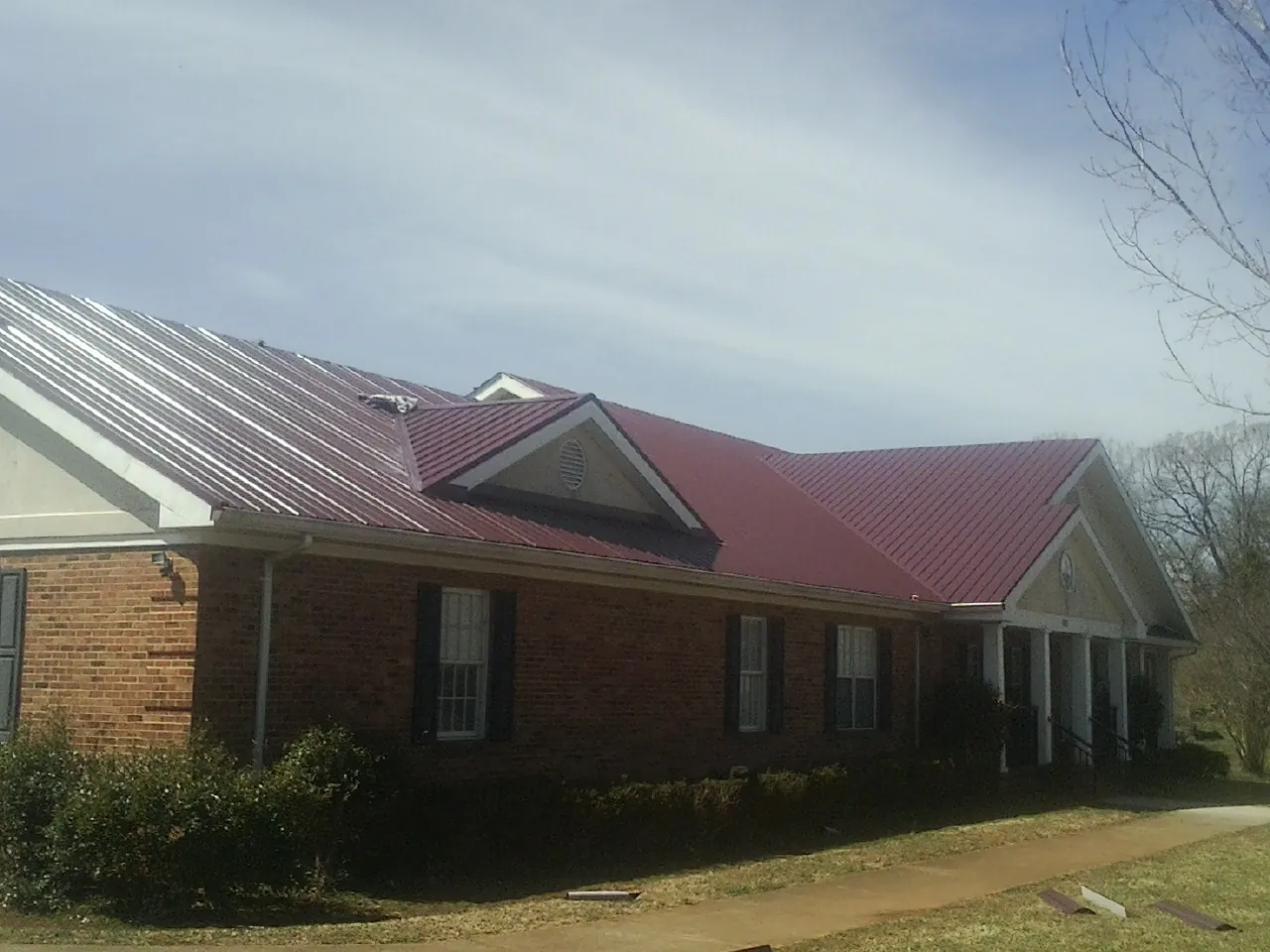 Red metal roof with gabled entries on a long brick building, from a Hail Damage Roof Repair job in Danielson
