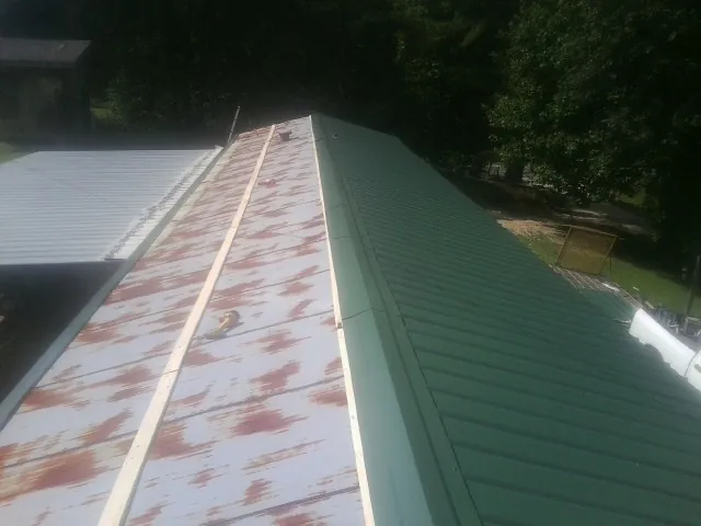 Old rusted panels beside newly installed green metal roofing — Wind Damage Roof Repair by Roofing Brothers in Danielson