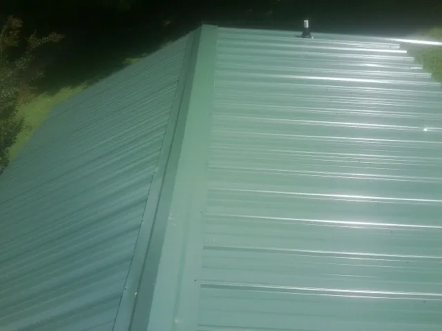 New green metal panels meeting at the ridge of a roof — Flat Roof Repair work by our crew in Danielson
