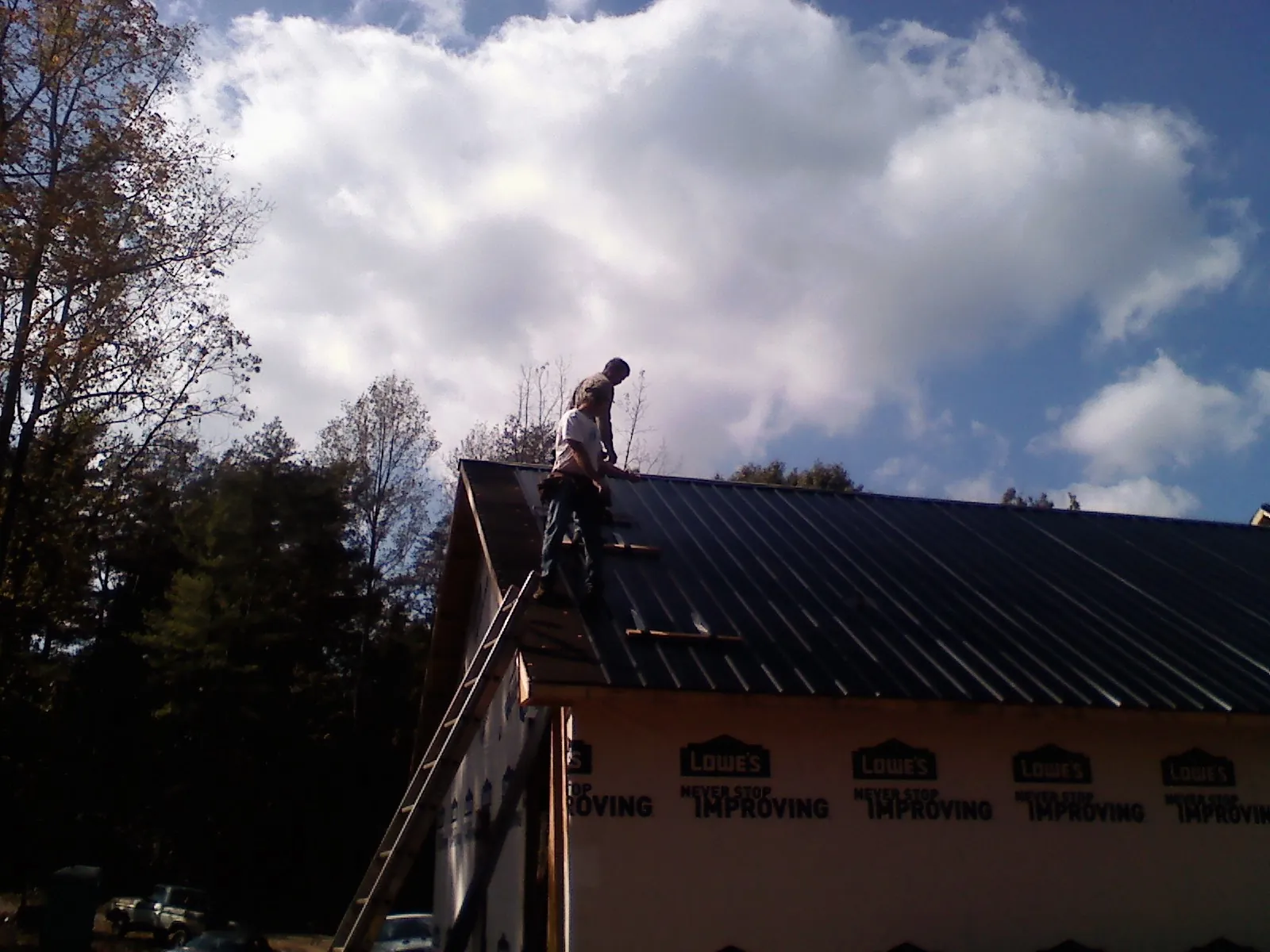 Roofer fastening dark metal panels high against a cloudy sky, from a Roof Inspection job in Danielson